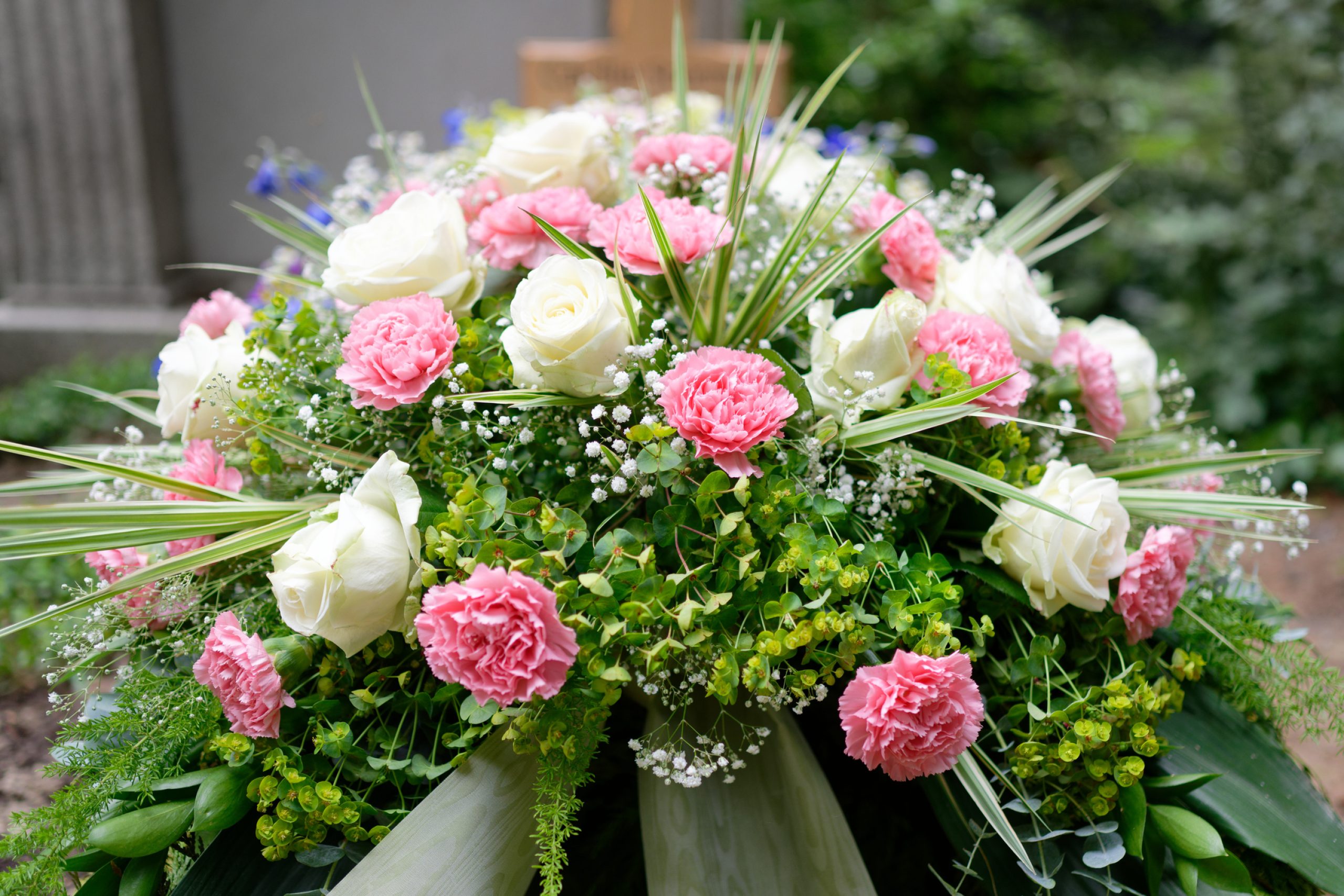 pastel funeral flowers on a grave in front of a wooden cross in blurred background